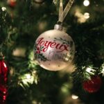 Close-up of a Joyeux Noel ornament on a decorated Christmas tree, glowing brightly.