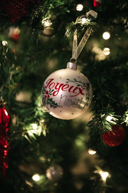 Close-up of a Joyeux Noel ornament on a decorated Christmas tree, glowing brightly.